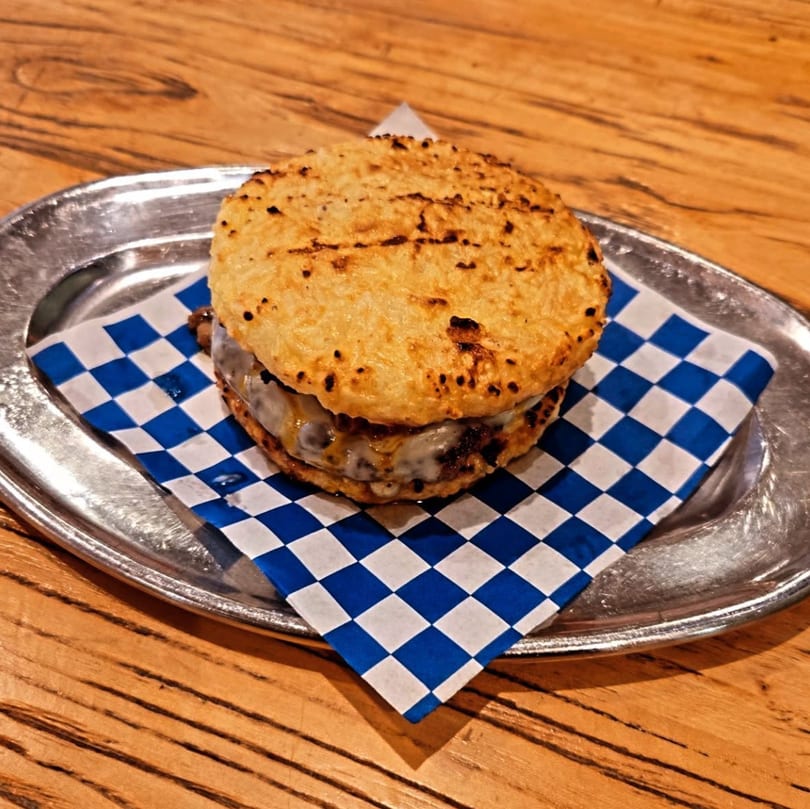 Zaab Burger's burger with a grilled rice bun, melted cheese, and meat on a checkered paper.