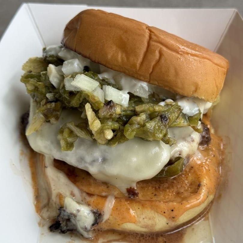 Zaab Burger's burger with melted cheese, green chiles, and diced onions in a white container.