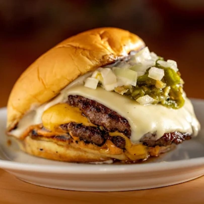 A Zaab Burger with two patties, melted cheese, diced onions, and green relish on a bun.