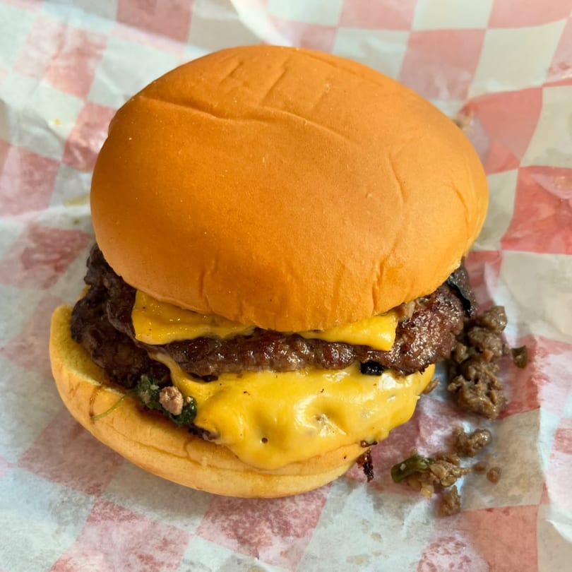 Zaab Burger's double cheeseburger with melted cheese and meat crumbles on checkered paper.