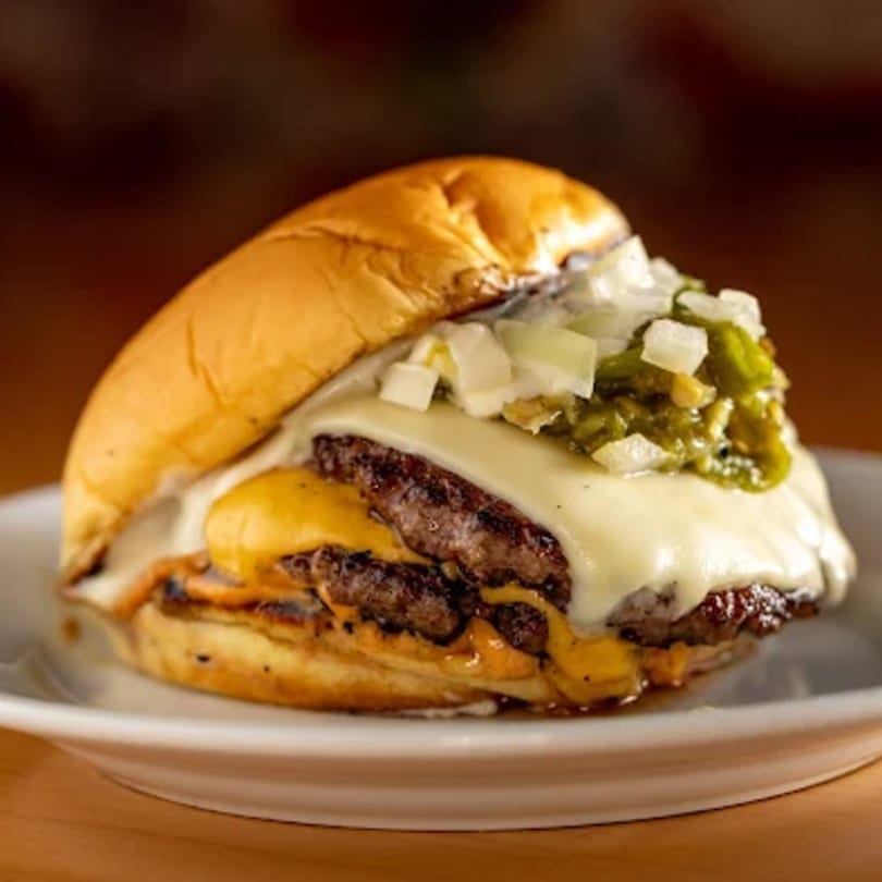 Zaab Burger's double patty burger with melted cheese, diced onions, and green relish on a white plate.